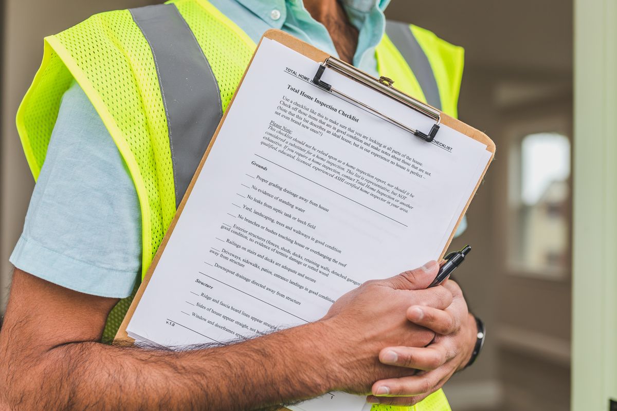 Home warranty inspection checklist on a clipboard held by an inspector in a yellow safety vest
